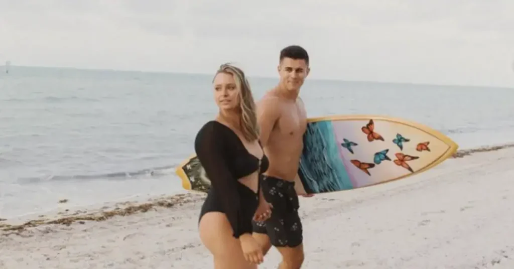 beach couple poses walking hand in hand with a surfboard