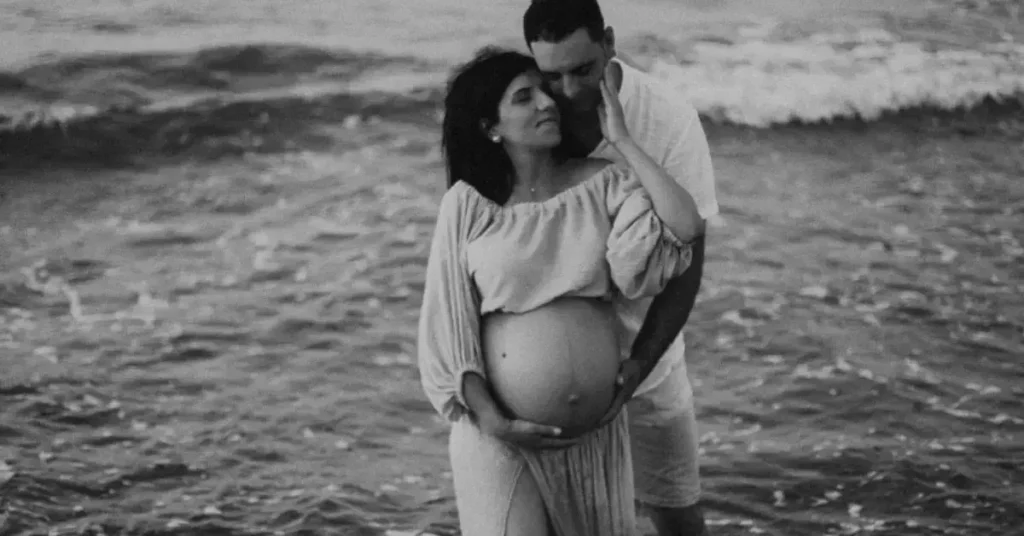 couple maternity poses hand on the belly in front of the water